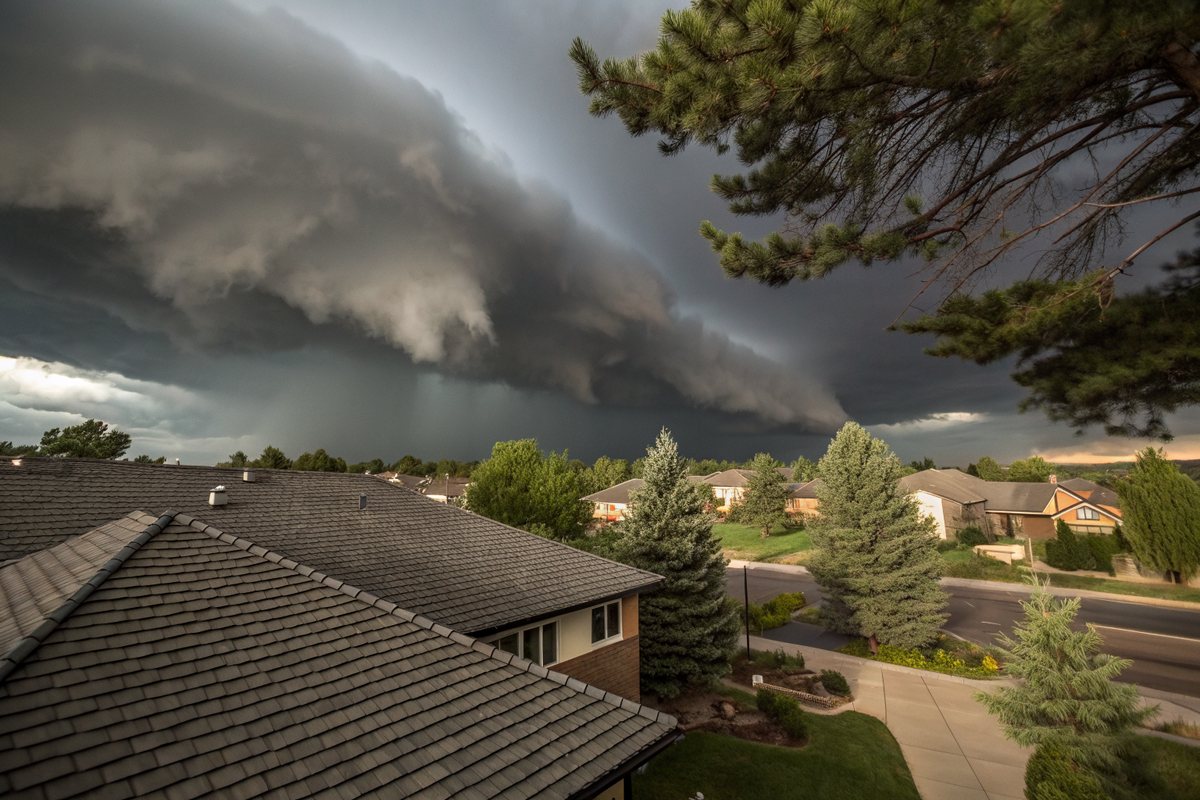 A dark shelf cloud rolling in over a neighborhood of shingle roofs